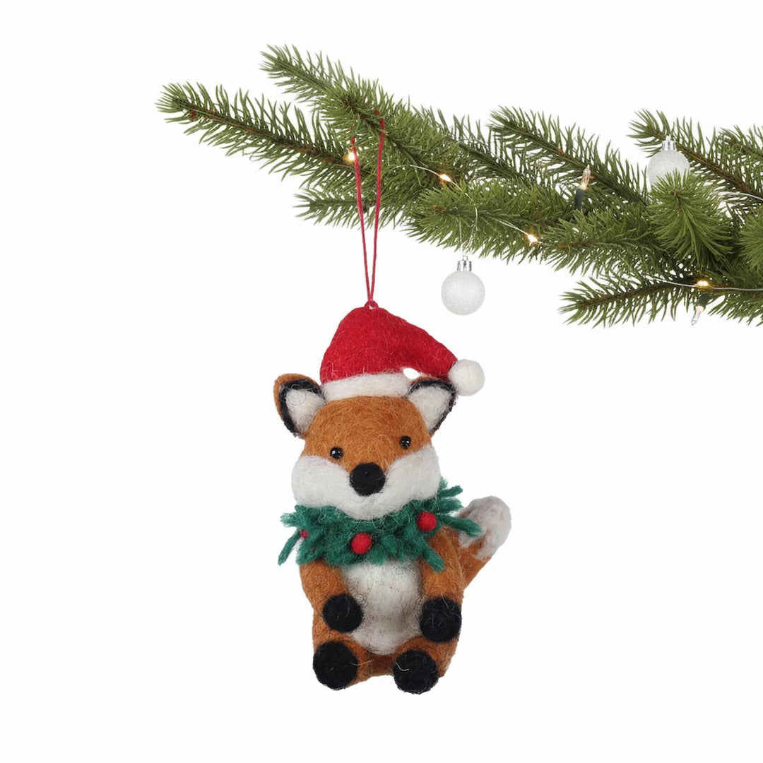 Felt fox ornament with a Santa hat and wreath hanging from a Christmas tree branch.