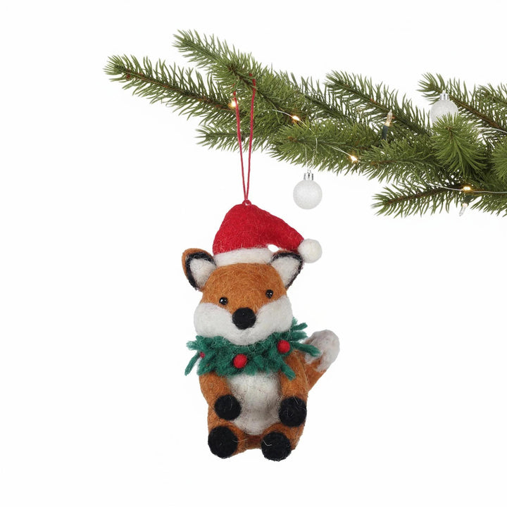 Felt fox ornament with a Santa hat and wreath hanging from a Christmas tree branch.