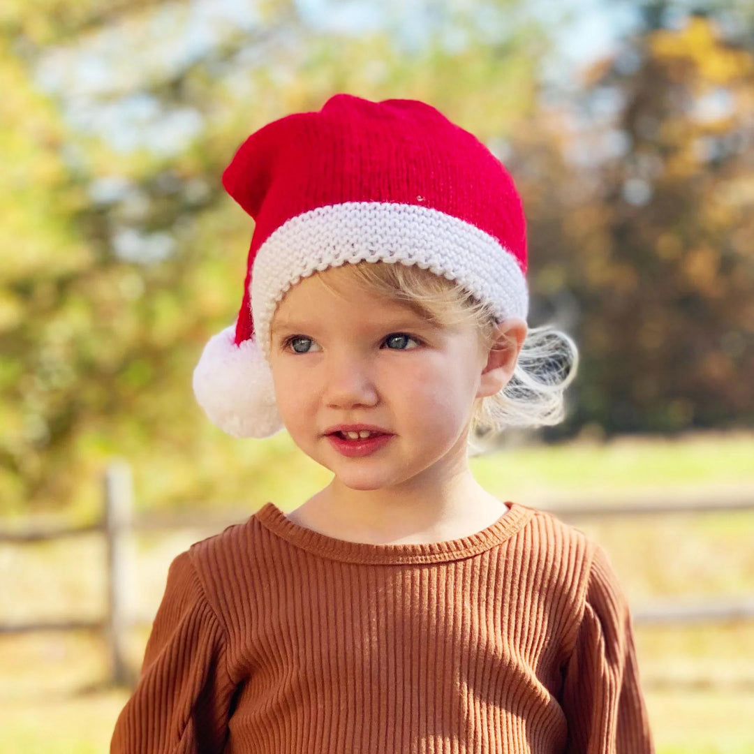 Child wearing a red Santa hat outdoors with a blurred natural background
