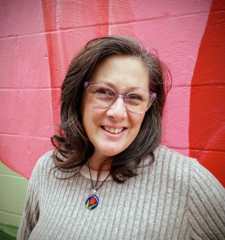 Woman wearing glasses and a sweater with a colorful tulip pendant against a pink and red striped background