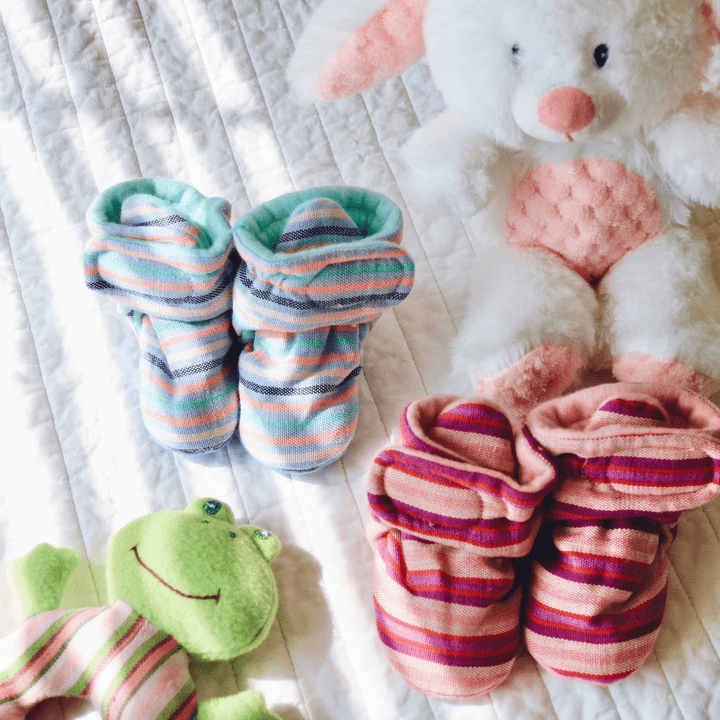 Pair of striped baby socks with a plush toy and frog toy on a textured surface