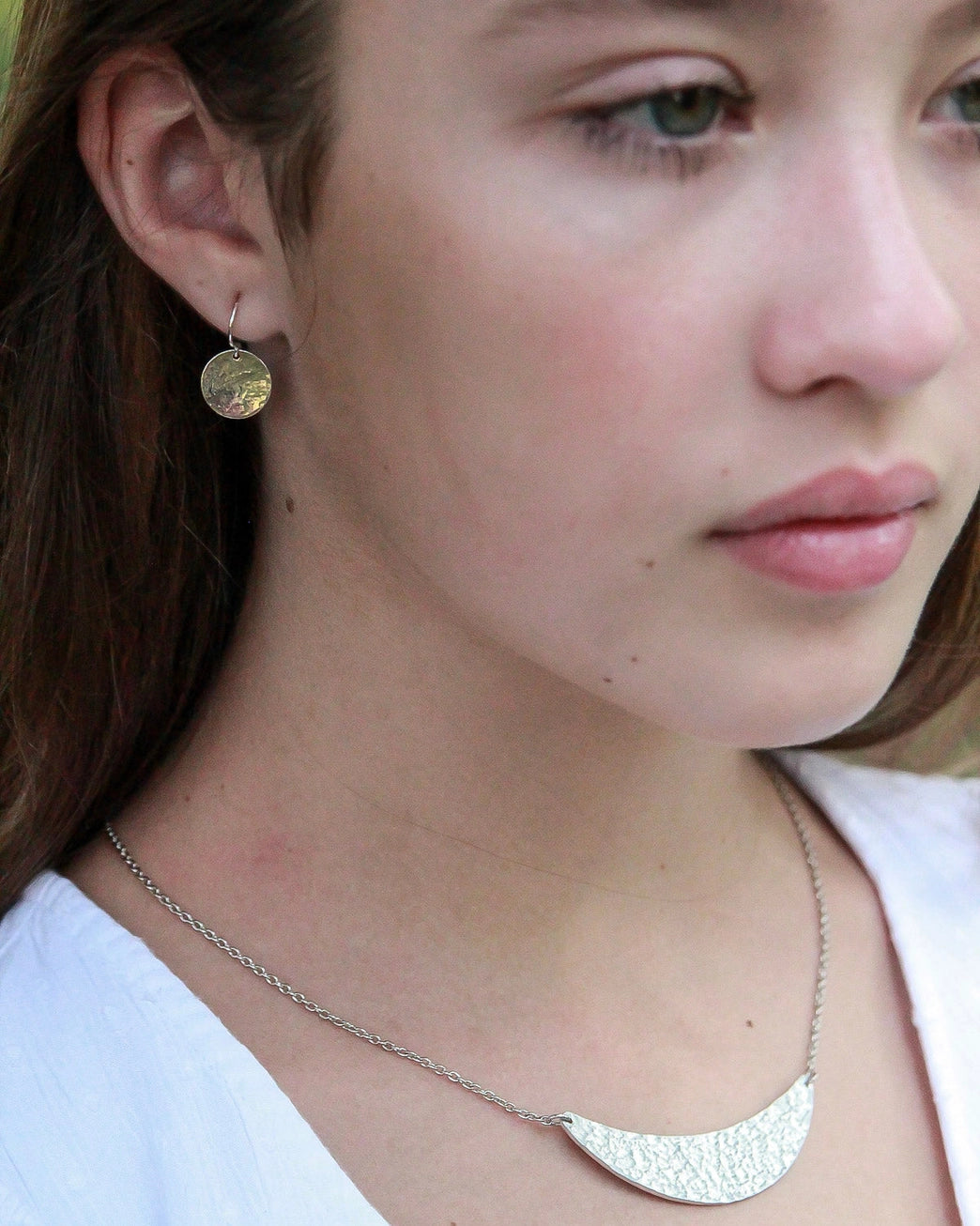 Close-up of a person wearing gold round earrings and a silver necklace.