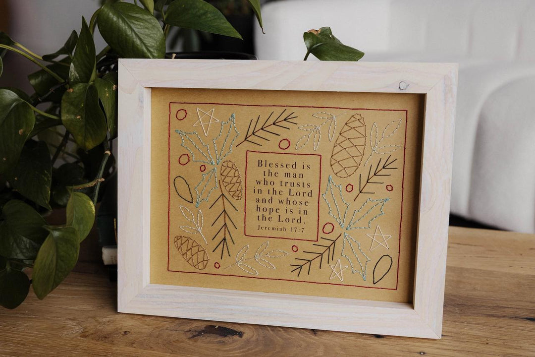 Framed embroidered artwork with decorative elements and text on a wooden surface.