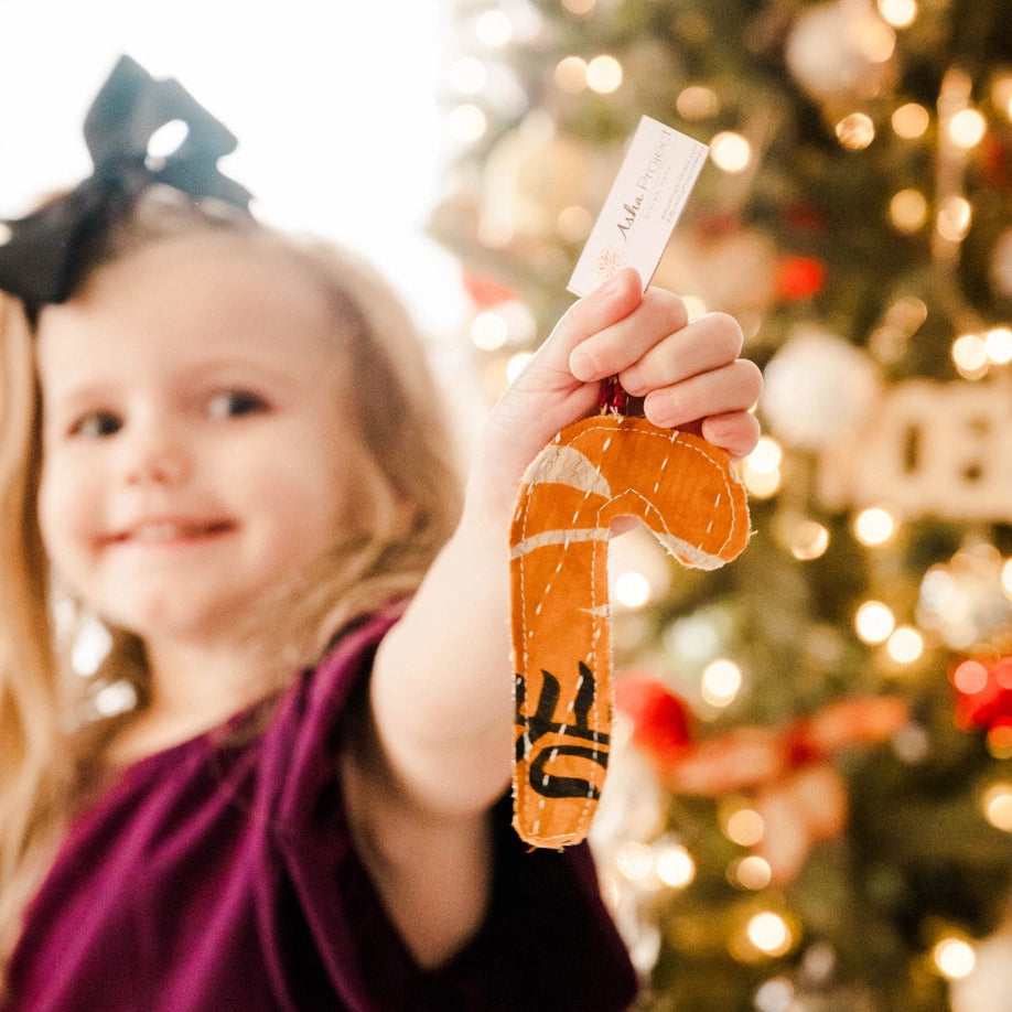 young girl holding out a kantha candy cane ornament