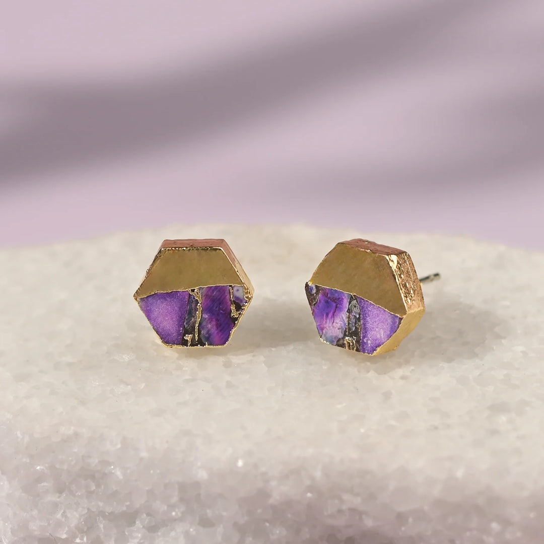 Hexagonal gold and purple earrings on a textured surface with a gradient background