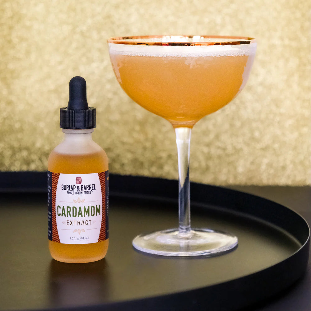 Bottle of Burlap & Barrel Cardamom Extract next to a cocktail with a gold background