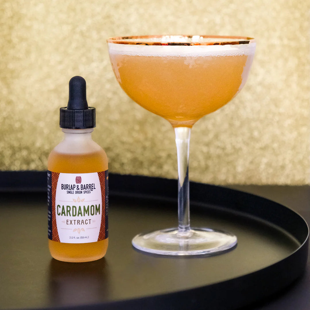 Bottle of Burlap & Barrel Cardamom Extract next to a cocktail with a gold background