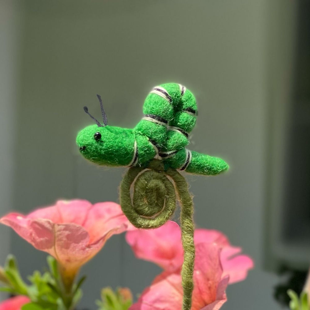 Green caterpillar plush floral stake on pink flowers with a blurred background