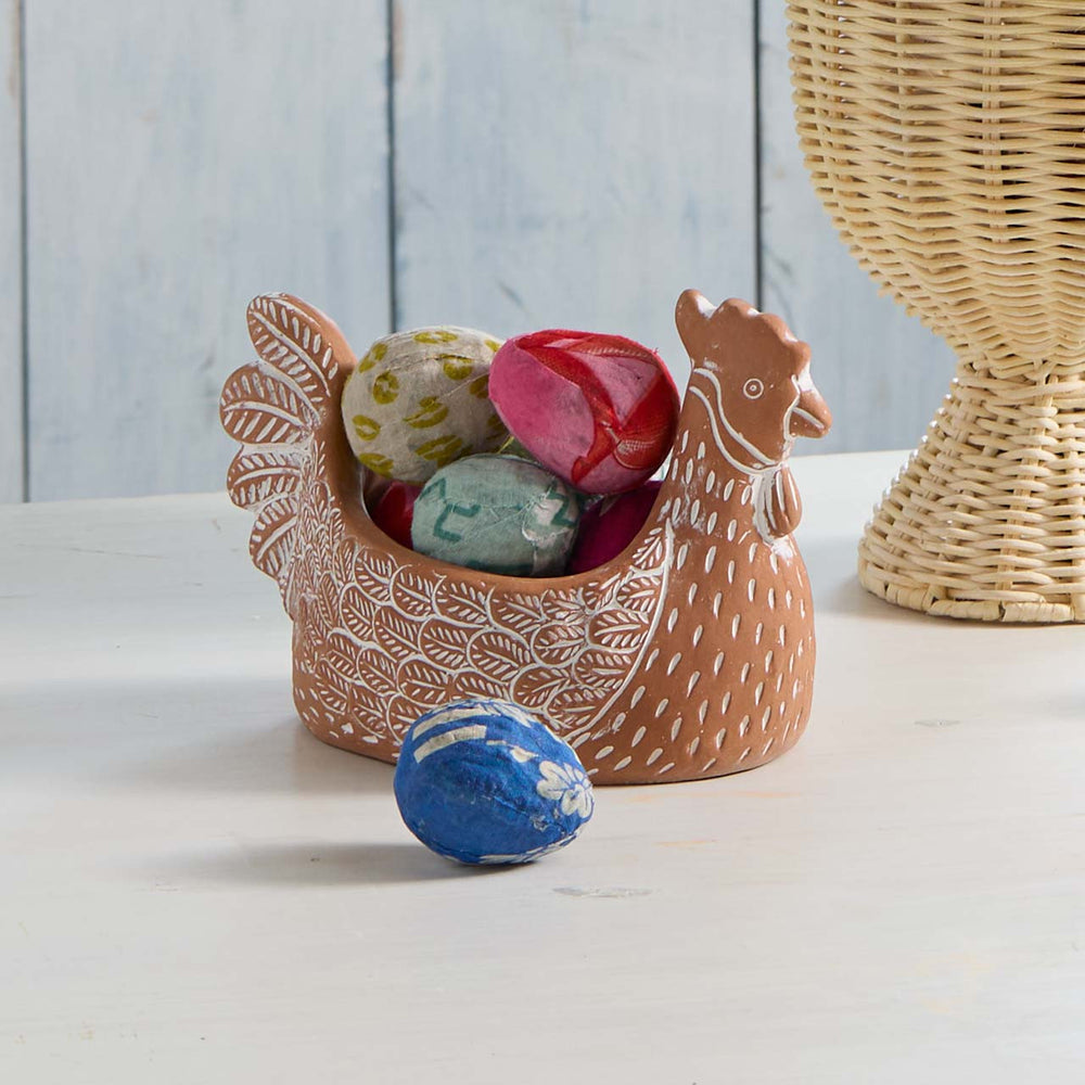 Decorative chicken-shaped container with colorful eggs on a light surface.