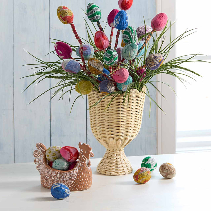 Decorative Easter arrangement with colorful eggs in a woven vase on a light surface.