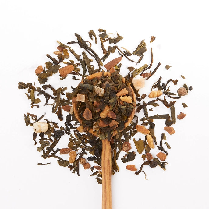 Wooden spoon filled with a mix of dried coconut green tea leaves on a white background