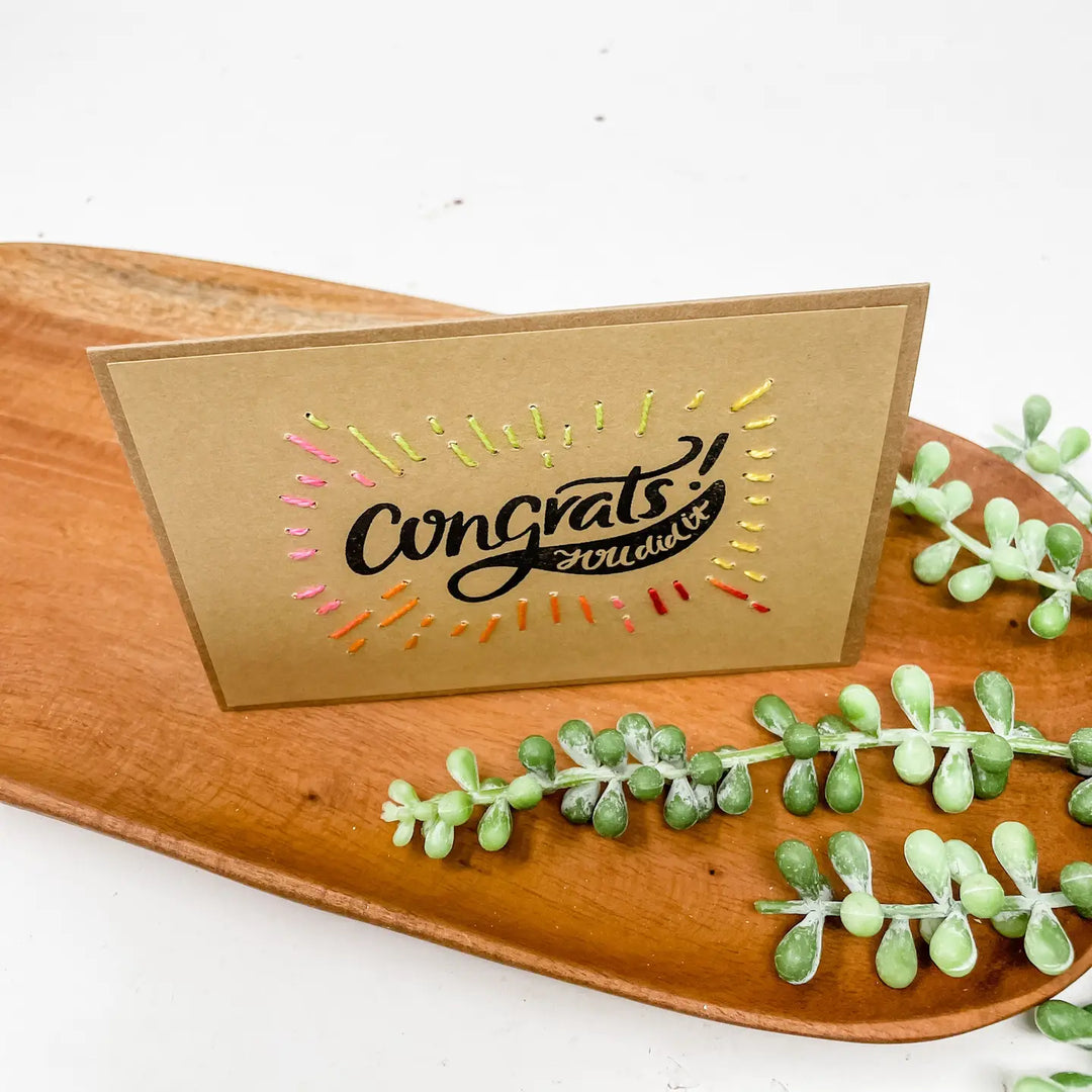 Kraft paper card with 'Congrats' text on a wooden tray with green plants