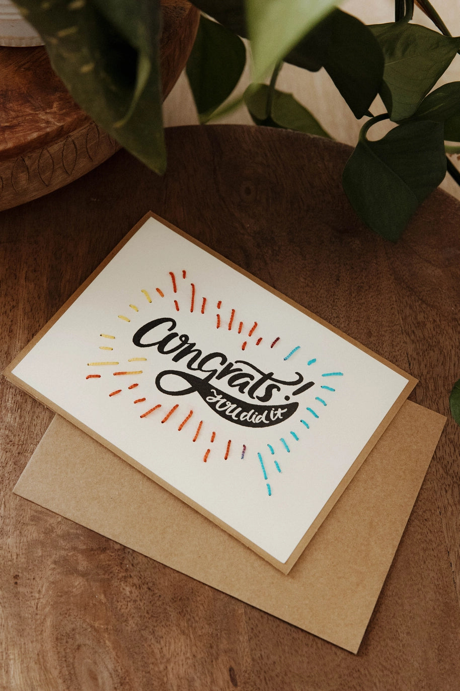 Greeting card with 'Congrats' text on a wooden surface with a plant in the background
