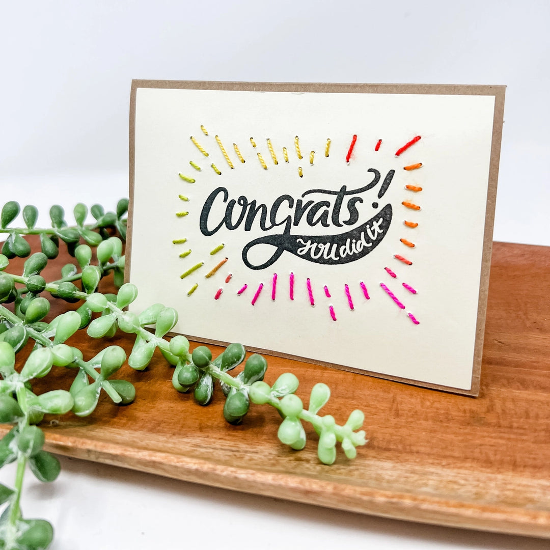 Greeting card with 'Congrats you did it!' text on a wooden surface with greenery