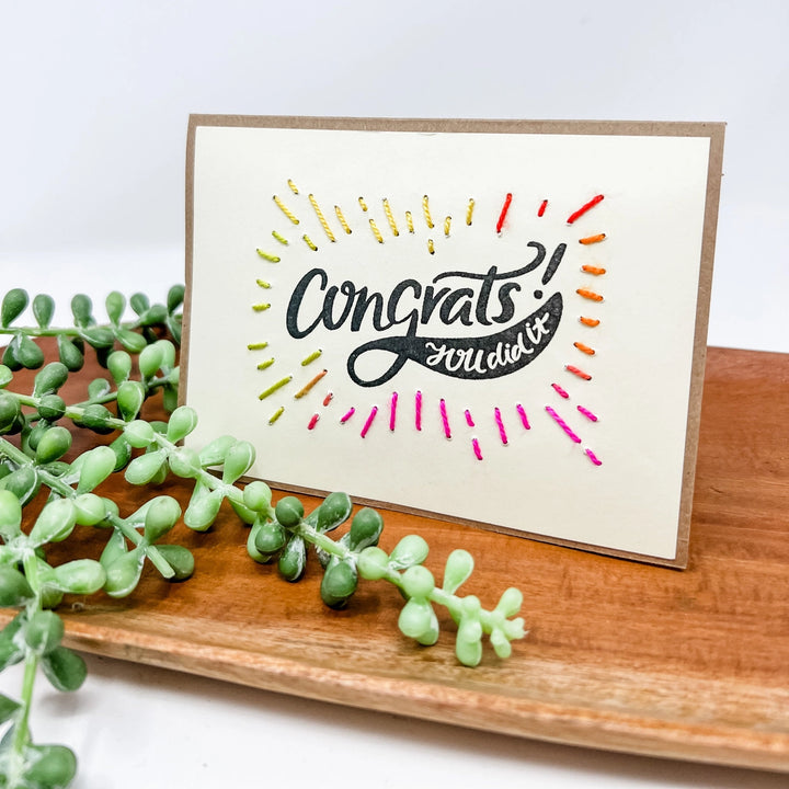 Greeting card with 'Congrats you did it!' text on a wooden surface with greenery