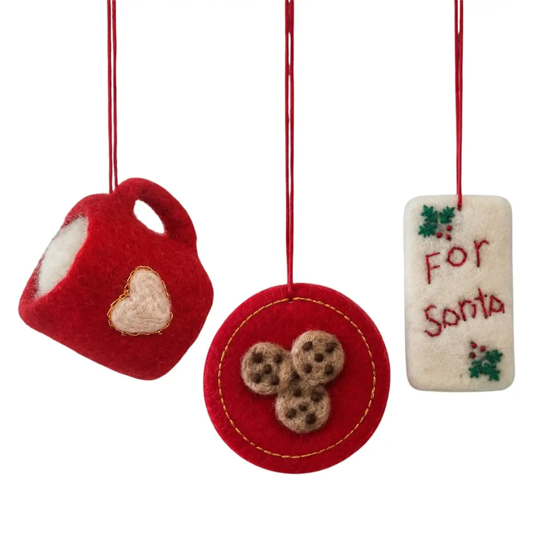 Three red and cream felt Christmas ornaments hanging by red strings on a white background: a teacup ornament with a cream heart, a round red ornament with three cookie details, and a cream rectangular tag reading 'For Santa' with small green holly accents.