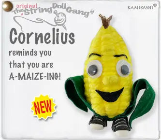 A string doll corn character toy labeled Cornelius from The String Doll Gang, with a bright yellow corn body, green fabric leaves, black-and-white striped feet, and a small brown top detail. The image includes printed branding and text on a white background.