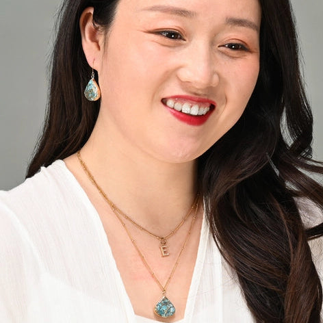 Woman with long dark hair wearing earrings and a necklace against a gray background