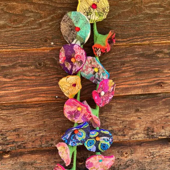 A handmade floral garland made of colorful fabric flowers with painted details, laid out on a rustic wooden surface.