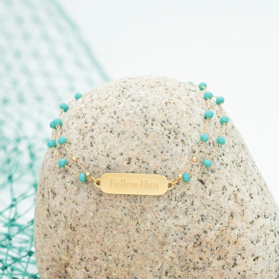 bracelet with turquoise beads and gold tag on a stone the background