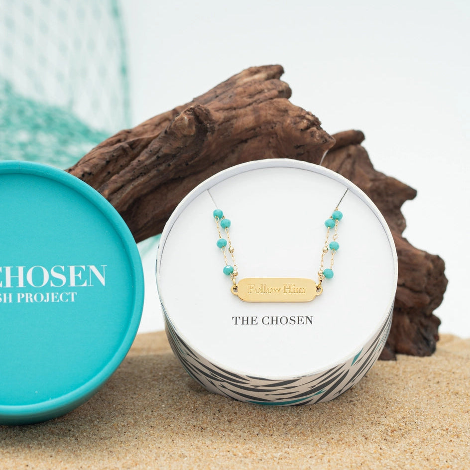 Necklace with turquoise beads in a 'The Chosen' box on sand with 'CHOSEN' branding.