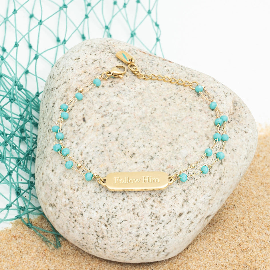 Gold bracelet with turquoise beads on a rock with teal netting in the background
