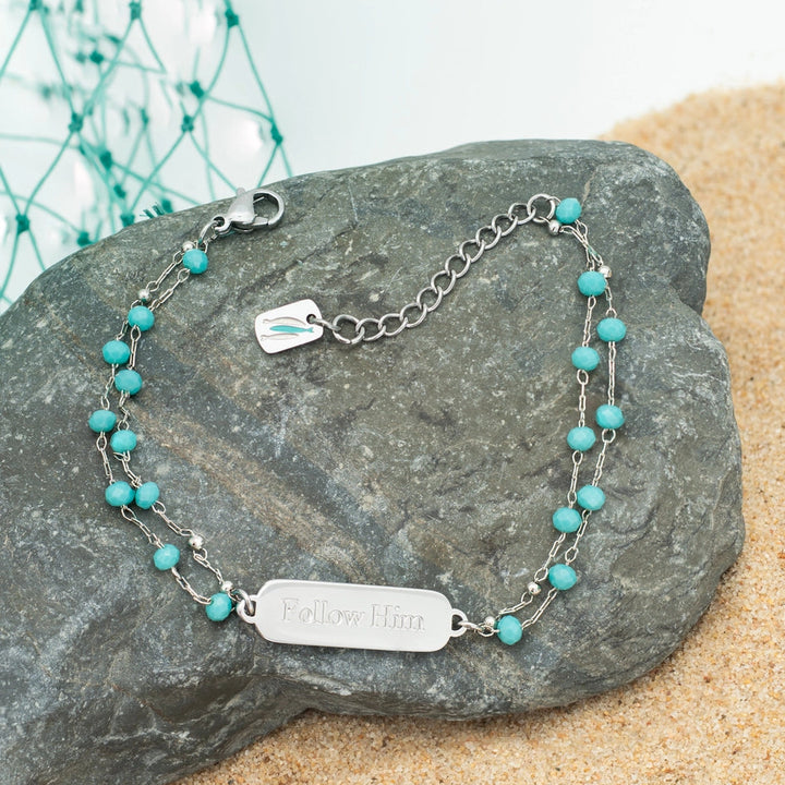 Turquoise beaded bracelet with silver tag on a stone surface
