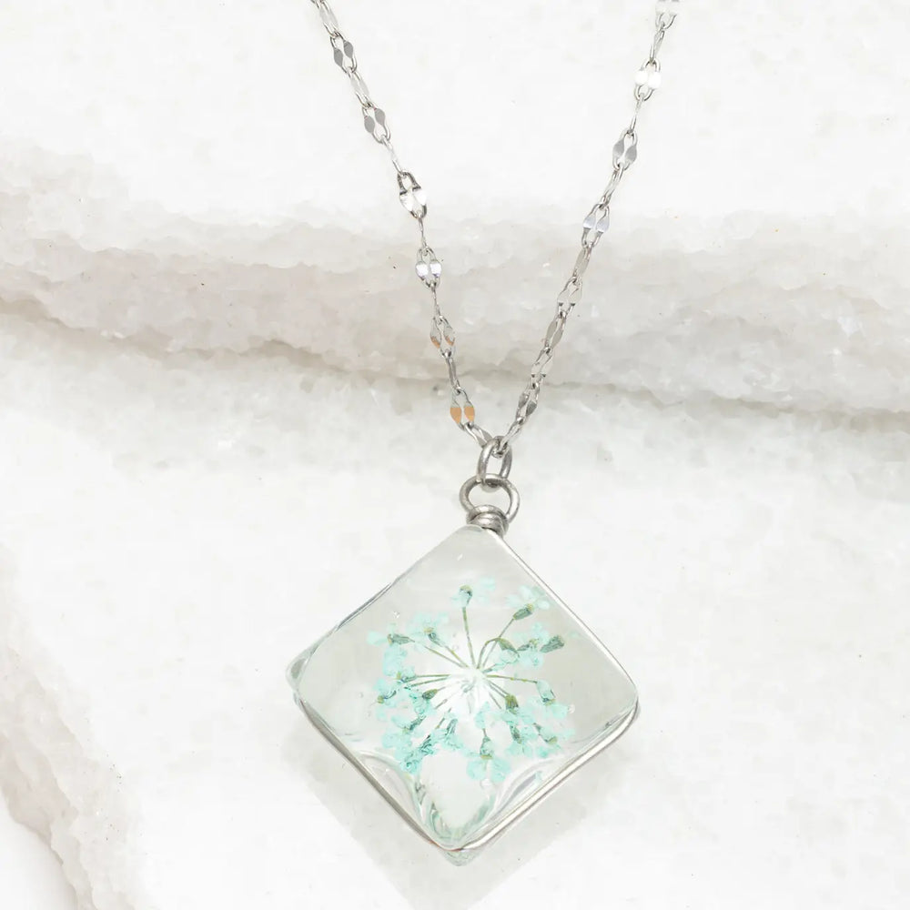 Necklace with a square pendant featuring a floral design on a marble surface