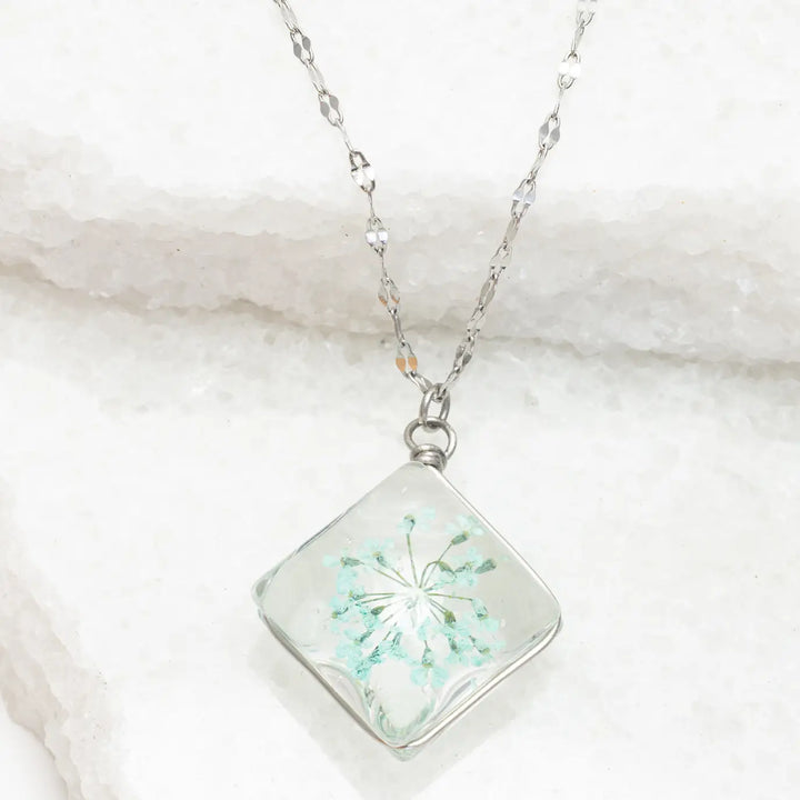 Necklace with a square pendant featuring a floral design on a marble surface