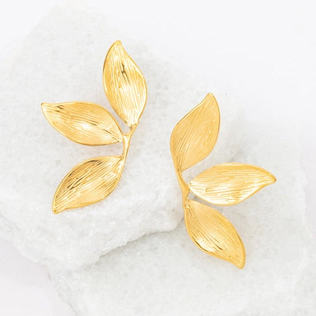 Gold leaf-shaped earrings on a white marble surface