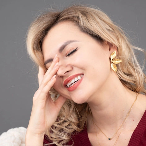 Woman wearing a red sweater and gold earrings with a gray background