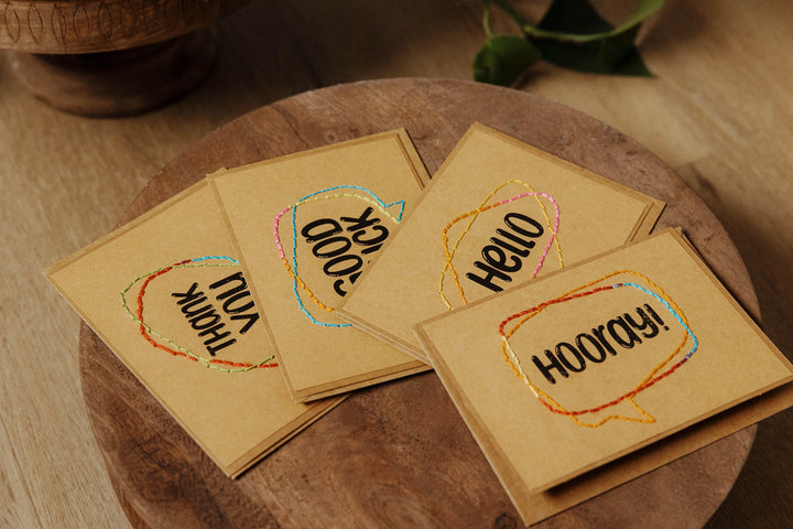 Four small greeting cards with embroidered text on a wooden surface