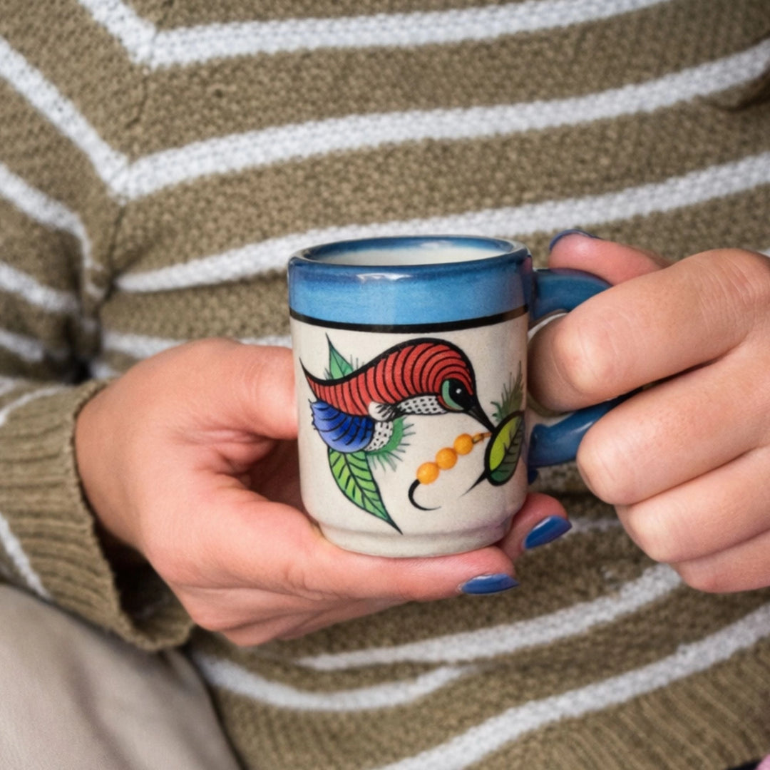 Person holding a colorful mug with a bird design, wearing a striped sweater.