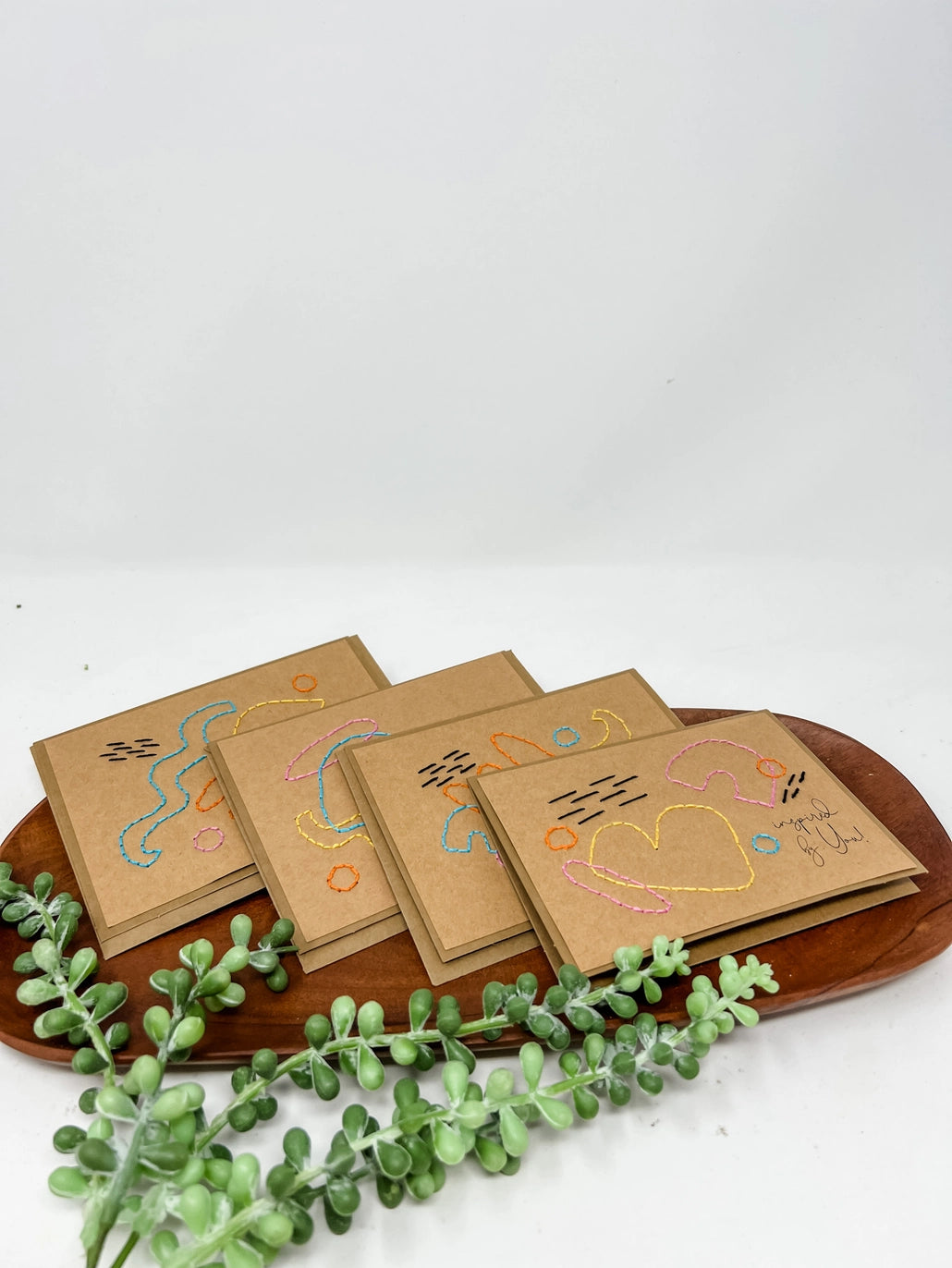Set of small brown cards with colorful designs on a wooden tray with green leaves.