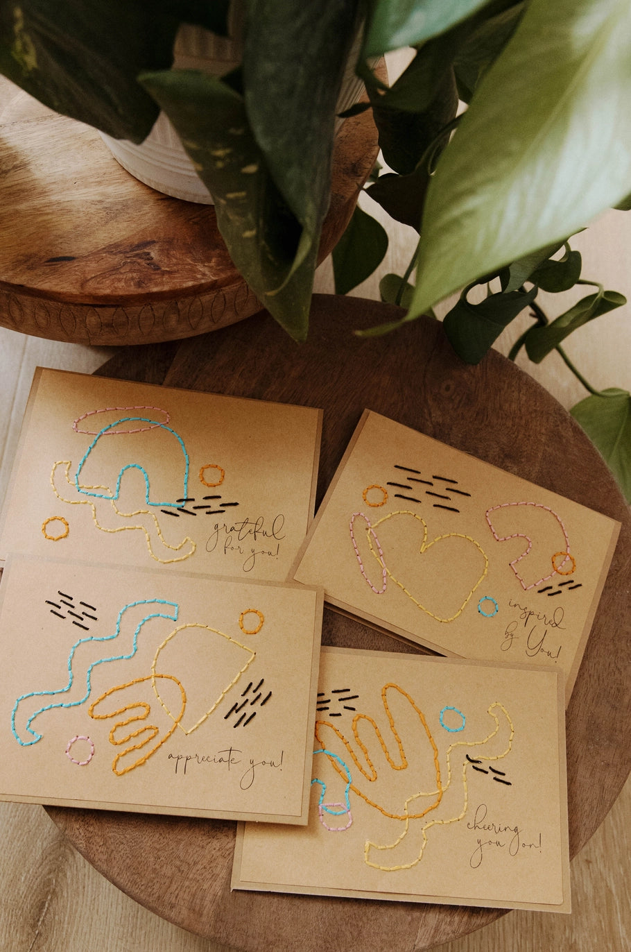 Embroidered cards on a wooden surface with plants in the background