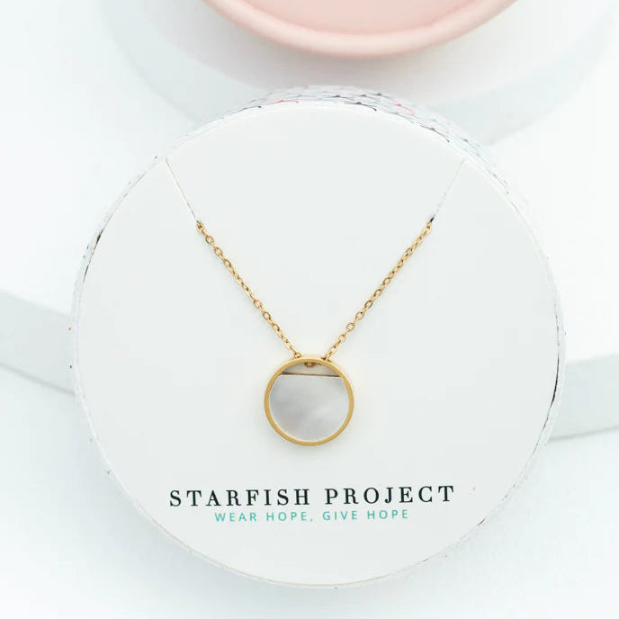 Gold necklace with a round pendant in a Starfish Project box on a white background