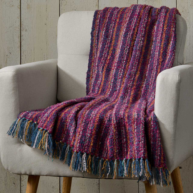 Multicolored striped blanket draped over a gray armchair against a wooden paneled wall.