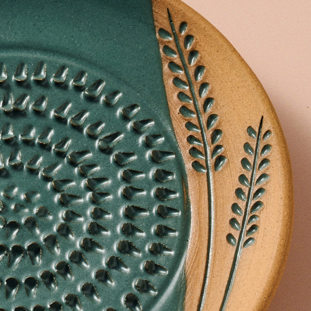 Close-up of a ceramic grater plate with textured design and wheat pattern on a terracotta background