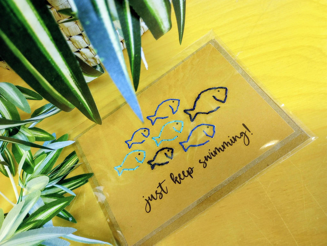 Kraft paper card with blue and black fish illustrations and text 'just keep swimming!' 