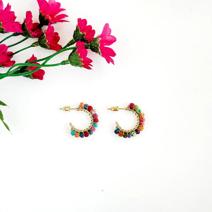 Colorful Kantha gold-plated hoop earrings with multicolored beads on a white background with pink flowers.