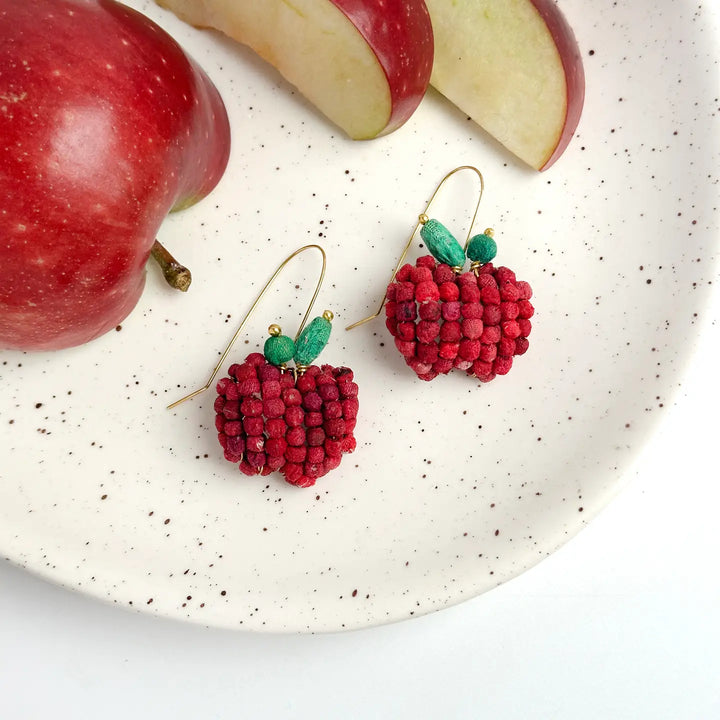 Red apple-shaped earrings on a speckled plate with red apples