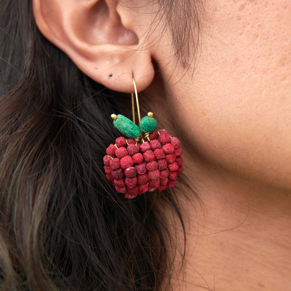Close-up of a person wearing a red apple earring with green leaves.