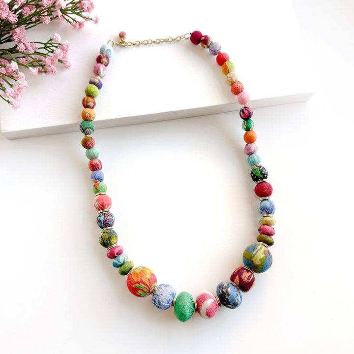 Kantha coterie necklace on white background with pink flowers.