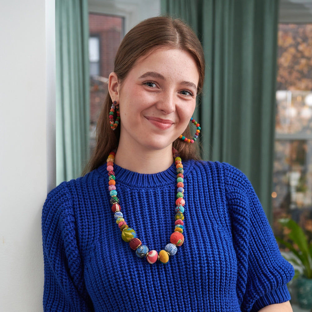Woman wearing a colorful kantha coterie necklace and blue sweater indoors