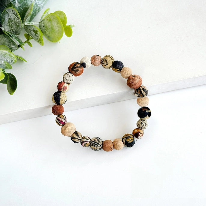 Multicolored beaded kantha bracelet on a white surface with green leaves in the background