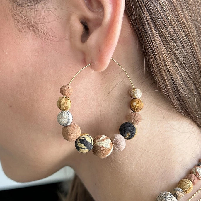Close-up of a person wearing a hoop earring with desertscape beads.