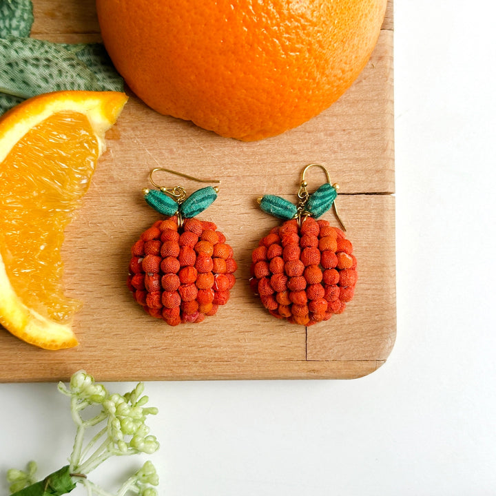 Orange-shaped Kantha beaded earrings on cutting board with orange slices
