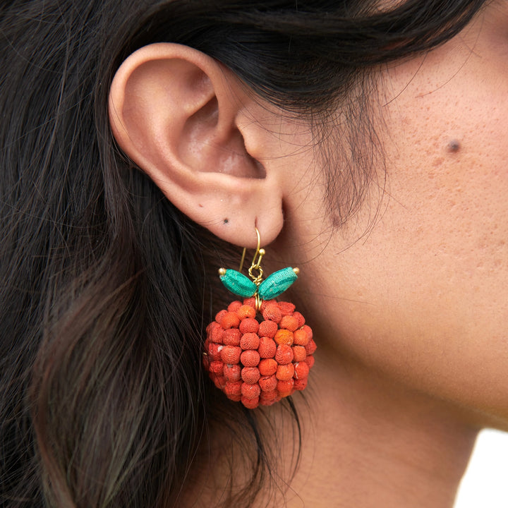 Close-up of an ear wearing orange shaped earring with green leaves.