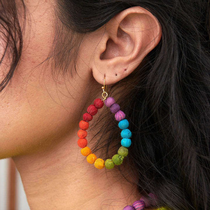 Close-up of a colorful beaded Kantha hoop earring worn by a person.