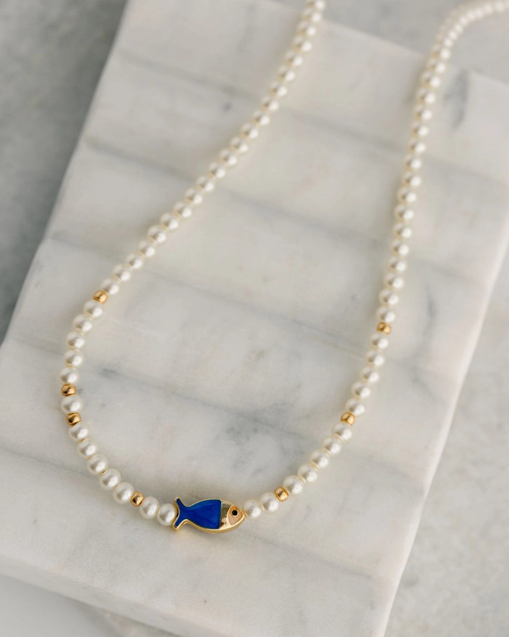 Pearl necklace with a blue fish charm on a marble surface